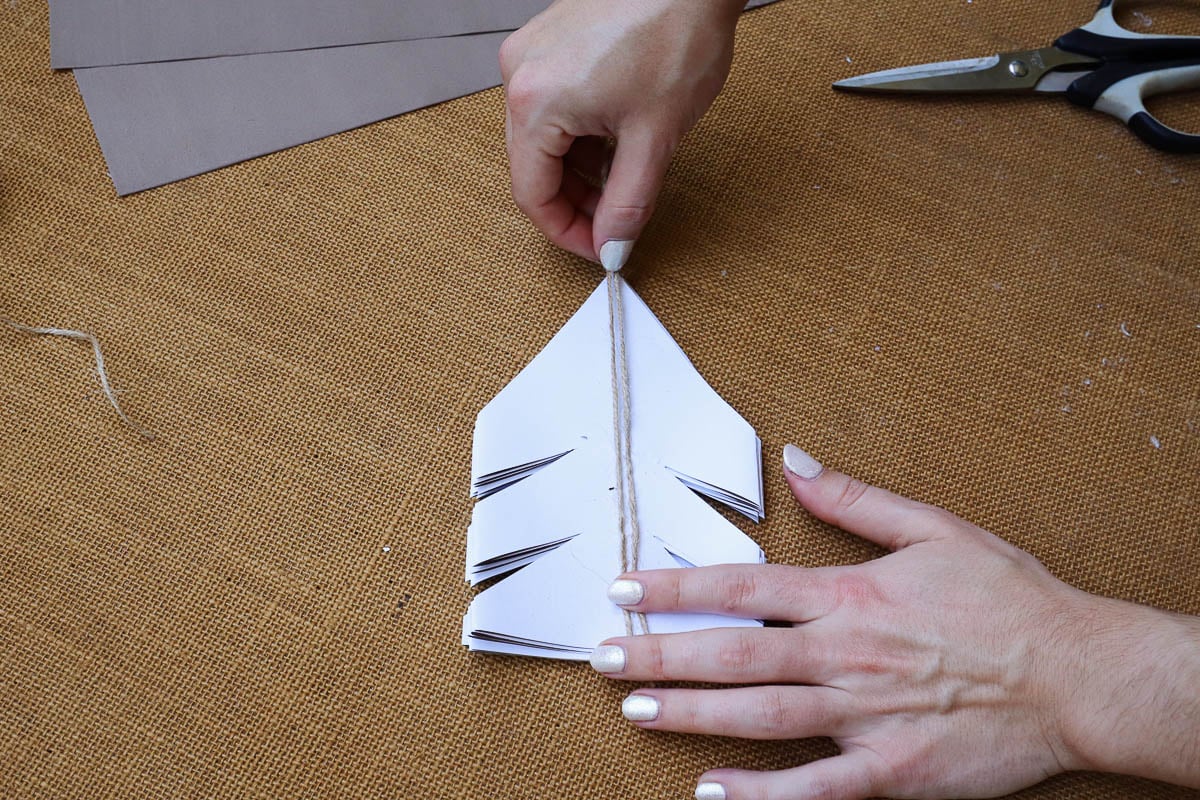 Woman's hand placing twine along folded pieces of paper.
