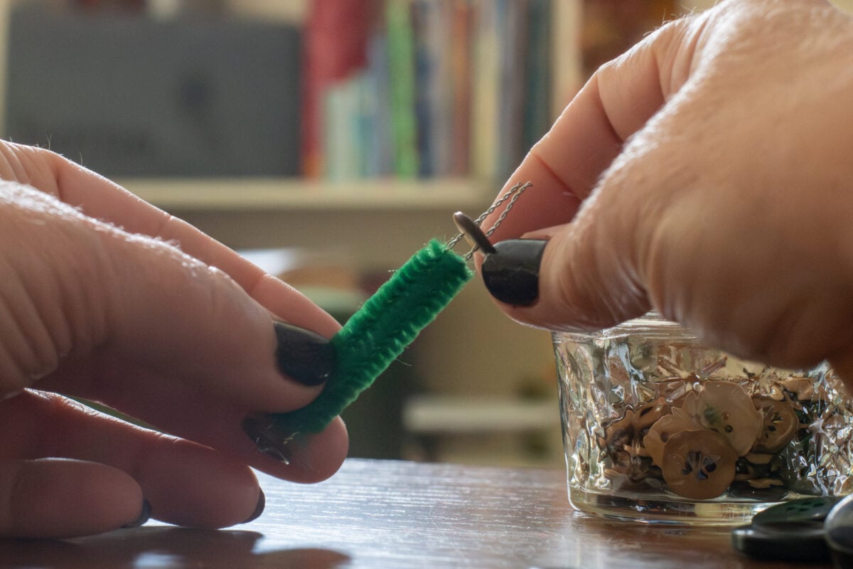Hands putting buttons on a pipe cleaner.