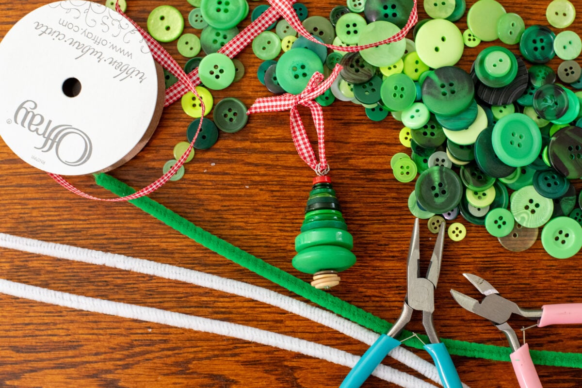 Buttons, pipe cleaners, ribbons, pliers and a button Christmas tree ornament. 