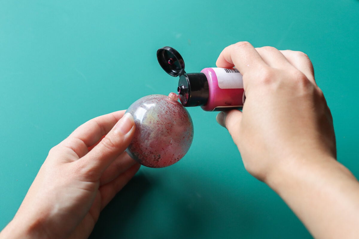 Hand pouring paint into Christmas bauble