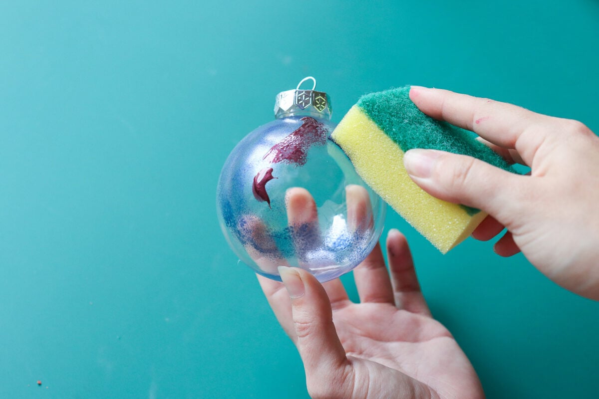Woman's hands sponging nail polish onto outside of Christmas bauble