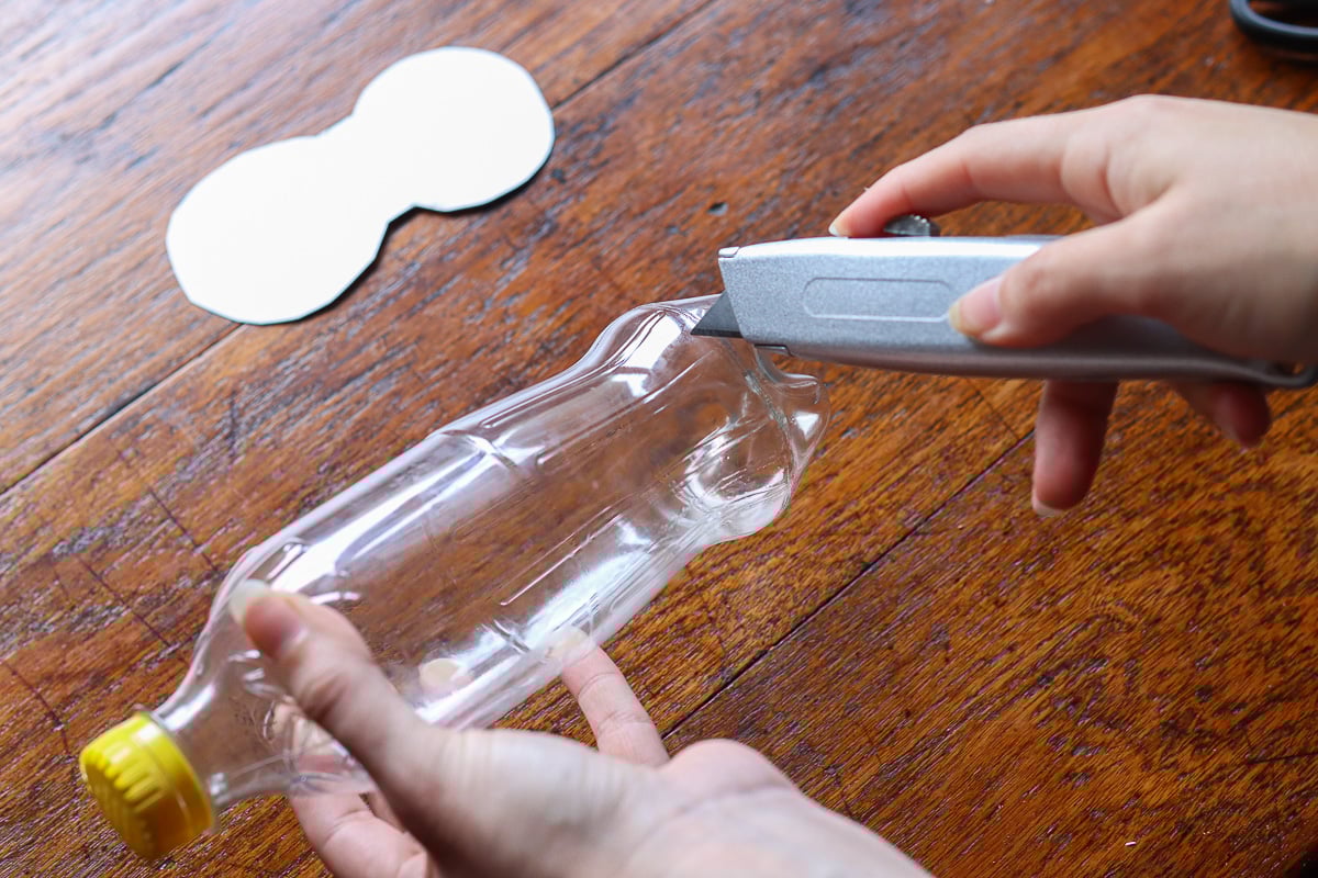 Woman's hand using box cutter to cut empty soda bottle