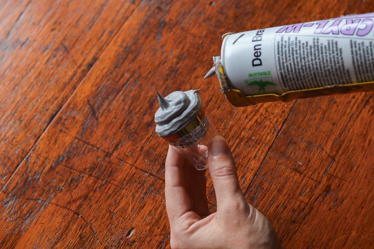 Woman's hand piping caulk onto plastic shot glass to make hot chocolate Christmas ornament.